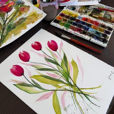 ציור מקורי: הקובץ il_fullxfull.6595581826_j7co.jpg מציג ציור בצבעי מים של שישה צבעונים ורודים עם עלים ירוקים על נייר כותנה לבן, מוקפים בפלטת צבעים, מכחולים בכוס ויצירת אמנות פרחונית נוספת על שולחן עץ כהה. מוסיף צבע וייחודיות לכל חלל.