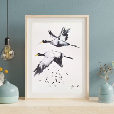 ציור מקורי: הקובץ il_fullxfull.6211388085_k0cc.jpg מציג ציור בצבעי מים ממוסגר של שני עגורים בשחור-לבן, המוצג על שולחן על רקע קיר כחול עם אגרטלים דקורטיביים ופרחים מיובשים. מוסיף צבע וייחודיות לכל חלל.