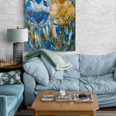 ציור מקורי: בסלון הנעים יש ספה בצבע תכלת, שולחן קפה מעץ ותמונה צבעונית על קנבס – ציור מופשט גדול של שתי פרות (il_fullxfull.6288197043_gewn.jpg) – התלויה על קיר לבנים לבן. מוסיף צבע וייחודיות לכל חלל.