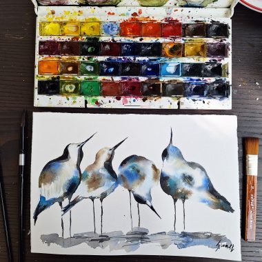 ציור מקורי: בתמונה il_fullxfull.6340098615_7jwi.jpg, פלטת צבעי מים עם צבעים עזים מונחת מעל ציור ציפורים מקורי המציג ארבע ציפורים מופשטות בצבעים כחול, חום ושחור על נייר כותנה לבן, כשלידו שני מכחולים. מוסיף צבע וייחודיות לכל חלל.