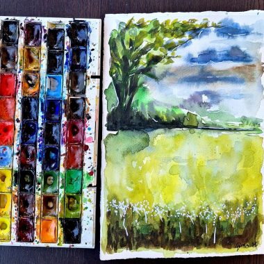 ציור מקורי: הקובץ il_fullxfull.6409825597_1c21.jpg מציג פלטת צבעי מים פתוחה, מחברת רישומים עם איור של שדה ירוק, פרחי בר, עץ גדול תחת שמיים מעוננים ומכחול על משטח עץ כהה. מוסיף צבע וייחודיות לכל חלל.