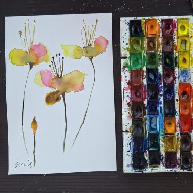 ציור מקורי: התמונה il_fullxfull.6509291498_esis.jpg מציגה ציור פרחים מופשט בצבעי מים בצהוב, ורוד וחום על נייר כותנה לצד פלטת צבעים עזה, המסודרת באלגנטיות על משטח עץ כהה. מוסיף צבע וייחודיות לכל חלל.