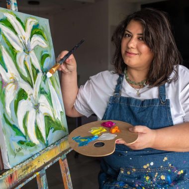 ציור מקורי: אישה בחלוק כחול מציירת חבצלות לבנות על בד איטלקי בשם 