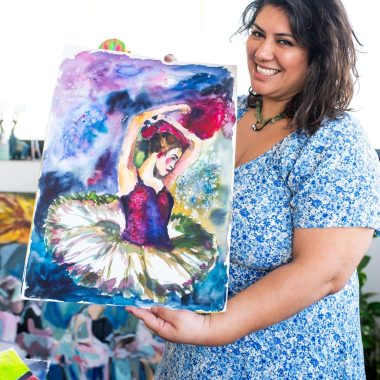 ציור מקורי: אישה בשמלה כחולה עם הדפס פרחוני מחייכת תוך שהיא מחזיקה את il_fullxfull.7079145278_rqka.jpg, ציור מקורי בצבעי מים של בלרינה עם טוטו על רקע מופשט וצבעוני. מוסיף צבע וייחודיות לכל חלל.