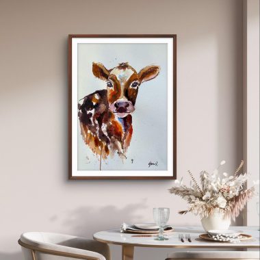 ציור מקורי: פינת אוכל עם שולחן לבן לשניים, כוסות וצלחות, כיסאות בהירים ותמונה של פרה בצבעי מים ממוסגרת על קיר בצבע בז'. אגרטל עם פרחים מיובשים משלים את המראה הכפרי. מוסיף צבע וייחודיות לכל חלל.